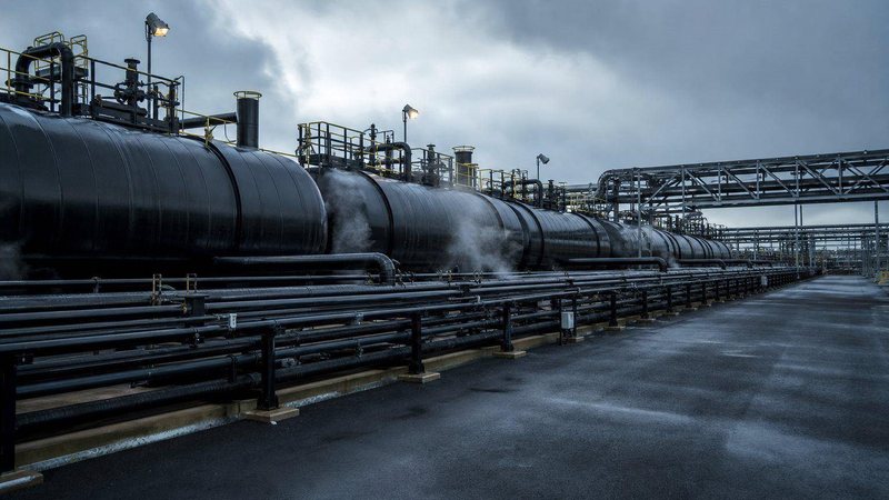 Insulated black bitumen tanks and heated pipelines at a terminal under a grey sky