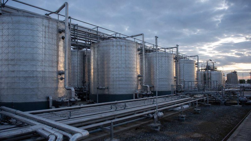 Row of stainless steel chemical storage tanks with pipe racks under a cloudy sky