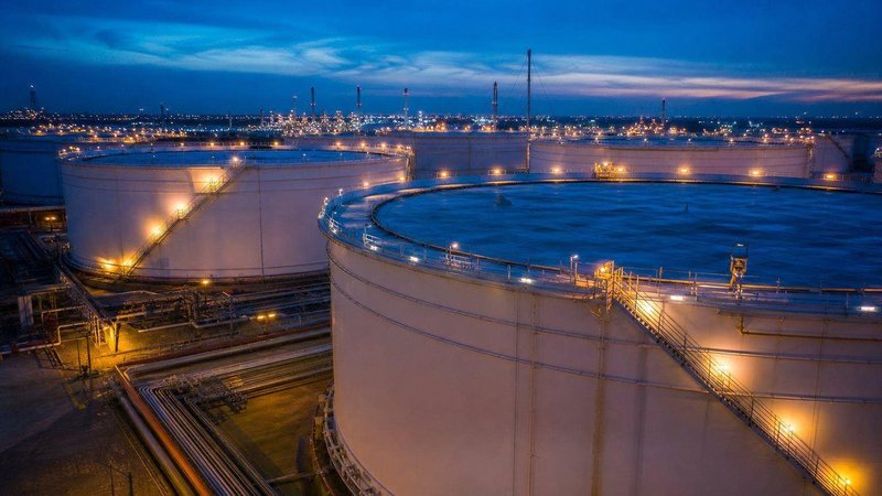Large crude oil storage tanks lit at dusk at a coastal terminal