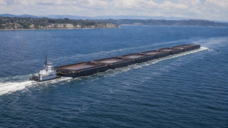 Tug pushing a long tank barge along a coastline